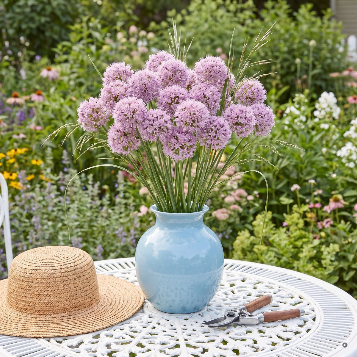 Geschnittene lavendelrosa Blütenkugeln von Allium 'Summer Beauty' in einer hellblauen Vase auf dem Gartentisch